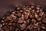 Läjä tummaksi paahdettuja kahvipapuja. Paahdetut kahvipavut ovat pavun puolikkaita. Kahvipavut ovat metallisessa astiassa.