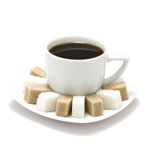 Valkoinen kahvikuppi täynnä mustaa kahvia. Kupin alla pieni kahvilautanen, jossa rivissä sokerinpalasia siten, että joka toinen on valkoinen sokeripala ja joka toinen ruskeaa sokeria.