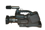 Valokuva muovisesta ja mustasta videokamerasta, joka on sivuttain. Kameran vasemmalla puolella linssi ja mikrofoni, oikealla olkapehmuste ja kantokahva.