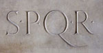Kivinen plakaatti, johon kirjoitettu roomalaisin tikkukirjaimin SPQR. Kirjainten välissä on pienet pisteet keskilinjassa. Q-kirjain on leveämpi kuin muut kirjaimet.