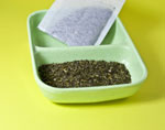 Vihreää teetä vihreässä kaukalossa ja vaaleanvihreää taustaa vasten. Vihreää teetä on jauheena ja sitä on myös teepussissa.