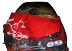 Punainen auto kuvattuna suoraan edestäpäin. Auton nokka on rutussa ja konepelti toiselta puolelta vääntynyt kieroon.