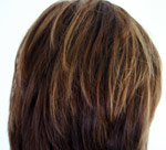 Pitkähiuksisen naisen tummanruskea peruukki, jossa on muutamia vaaleampia hiussuortuvia. Peruukki on kuvattu takaapäin.