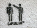 Seinägraffitti, jossa kaksi ihmishahmoa seisoo sanan Capitalism(tm) yllä siten, että vasemmanpuoleinen hahmo on kädet sivuilla ja oikeanpuoleinen osoittaa käsiaseella toista päähän.