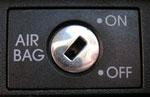 Mustaa pohjaväriä vasten jonkinlainen valikko, jossa keskellä rautainen avaimenreikää muistuttava vipu ja vasemmalla puolella lukee Airbag ja oikealla puolella On / Off.