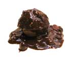 Valokuva suklaapallosta, jonka seassa suurai suklaan peittämiä pähkinöitä ja muita mötiköitä. Suklaapallo on sulanut.