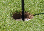 Tasaiseksi ja hyvin lyhyeksi leikattu vihreä ruoho, jonka keskellä kuoppa golfpalloa varten. Kuopan keskellä musta golfradan keppi.