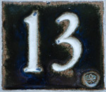Kuva rautaisen tai metallisen muotin sisälle maalatusta luvusta 13, jonka ympärillä oleva metalliaihio on musta. Kuvan oikeassa laidassa jonkinlainen koristeellinen leima tai muu merkki 13:n vierellä kuin pisteenä.